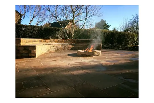 Autumn Brown Sandstone patio with built-in seating and a central fire pit, set in a sunny garden.