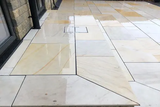 A close-up of a wet Mint Smooth Sandstone patio, highlighting its natural veining and warm hues