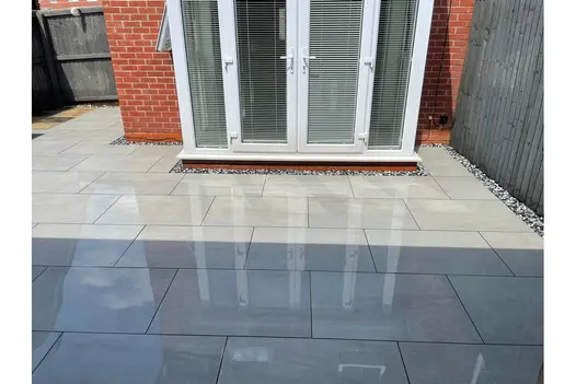 A contemporary glass door extension is complemented by smooth grey porcelain paving, creating a stylish and modern outdoor area.