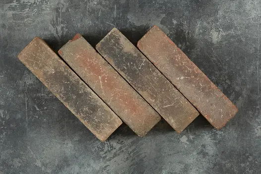 4 Abbey Dark Multi clay pavers laid edge-on in a slanting row against dark background. Free UK delivery available.