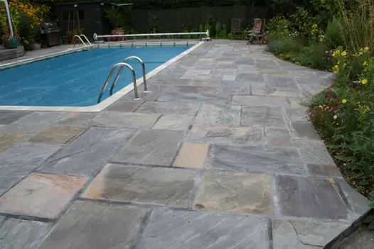Tumbled Black Sandstone paving with soft, weathered edges laid around a swimming pool, showing varied charcoal and grey tones.