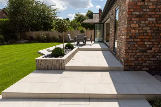 Patio laid with Allora Bianco 600x600mm porcelain tiles, blending seamlessly with the lush green lawn and outdoor seating area.