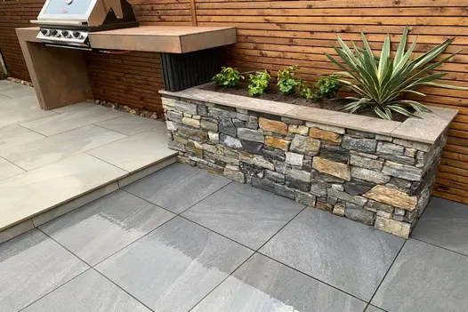 A stylish garden setup with a built-in barbecue, raised stone planter, and Allora Nero porcelain paving.