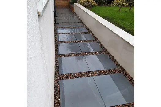 A sleek outdoor walkway featuring large-format Allora Nero porcelain stepping stones set in decorative gravel.