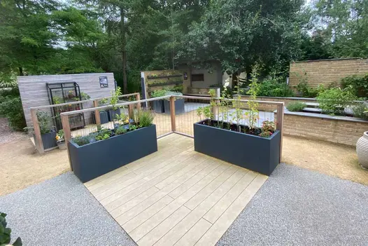Amber DesignBoard Composite Decking forming a central decked platform in a contemporary garden, surrounded by grey planters, gravel pathways, and modern balustrades.