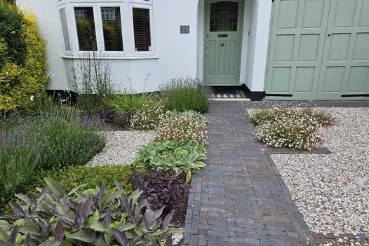 Ancona Clay Brick Pavers forming a neat, traditional pathway to a front door, with rich multi-tonal bricks complementing surrounding cottage-style planting and gravel borders.
