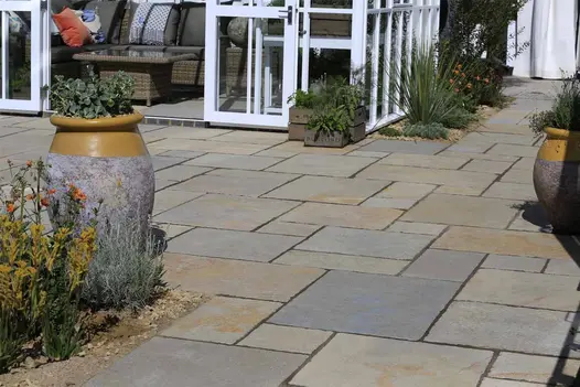Antique Yellow Limestone Project Pack paving laid in a mixed-size pattern, creating a warm natural stone patio beside a garden room with planted borders and feature pots.