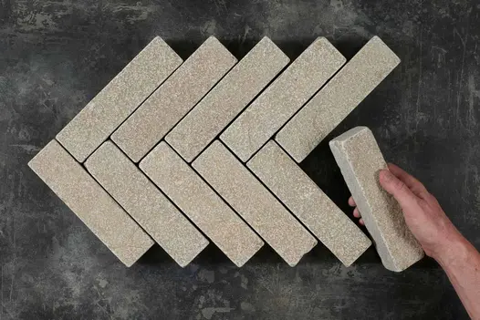 Hand places 11th stone paver at end of 5 courses of 2 Antique Yellow limestone patio bricks in herringbone pattern.