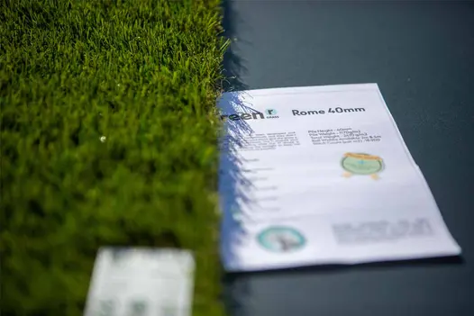 A section of artificial grass with a Rome 40mm product leaflet partially visible.