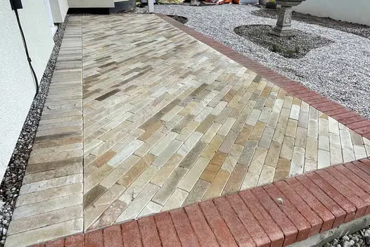 Tumbled Mint Sandstone Brick Pavers laid in a herringbone pattern with soft cream and beige tones, bordered by red clay bricks.