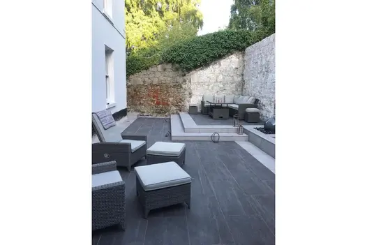 Contemporary patio using Overland Dark Porcelain Paving, paired with rattan furniture and raised walls.
