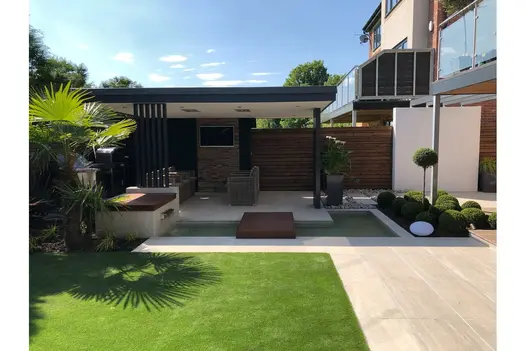 Stylish patio area laid with Overland Sand 900x450 Porcelain Paving, framed by lush planting and a contemporary pergola.