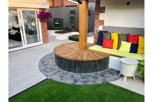 Playful outdoor space with Overland Silver 900x450 Porcelain Paving, circular decking and colourful seating.