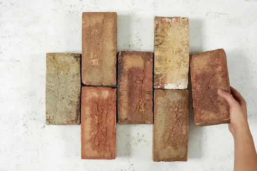Hand adds brick to right side of 6 Cotswold Blend clay pavers arranged in vertical rows of 1 or 2. Free UK delivery available.