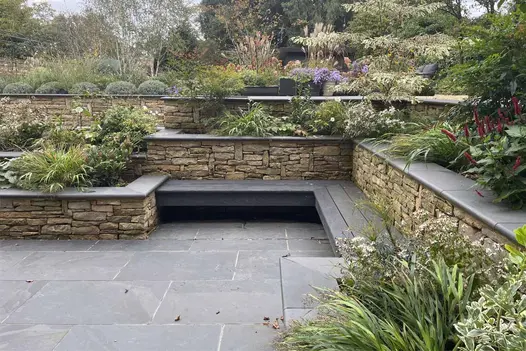 Brazilian Black Slate paving and step treads used in a tiered garden with dry-stone retaining walls and lush planting.