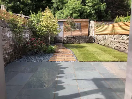 Brazilian Grey Slate paving used on a contemporary patio overlooking a lawn and timber-edged gravel path leading to a garden outbuilding.