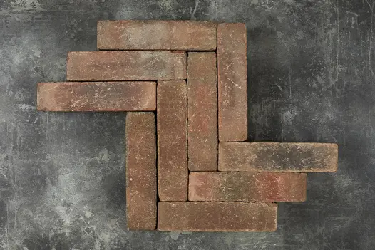 10 Abbey Dark Multi clay pavers laid in a herringbone pattern against a dark background, showing bricks’ tones of red and grey. 