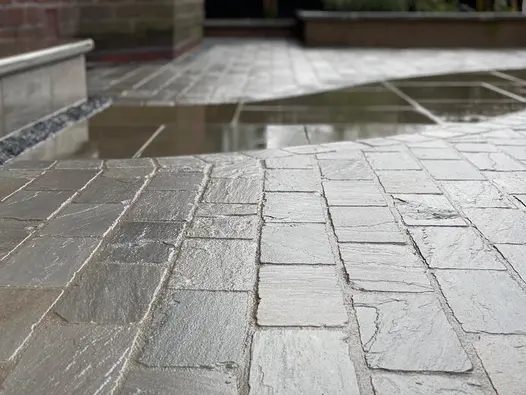 Kandla Sandstone Setts in varied grey tones laid in an irregular pattern, shown wet with a natural riven texture and tumbled edges.