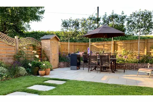 Kota Brown Limestone Paving forming a warm-toned patio in a landscaped garden, surrounded by planting, outdoor furniture, and a wooden shed.