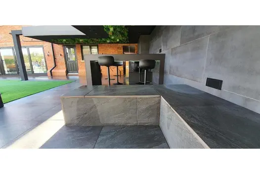Contemporary patio with grey porcelain tiles, bench seating, and bar area adjoining a modern red-brick home.