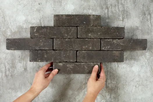 2 hands displaying nine charcoal grey brick pavers laid in jack-on-jack pattern, showing colour and texture.
