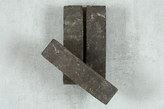 One Charcoal Grey Clay Paver is placed on top of two of the same brick pavers showing off colour and texture.