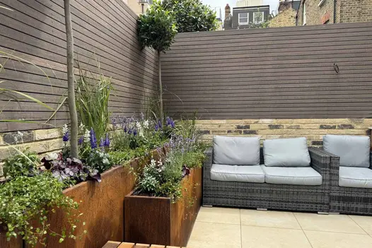 Chestnut Composite Fence Battens used to create warm-toned horizontal privacy screening in a courtyard garden, complementing brickwork and raised corten steel planters.