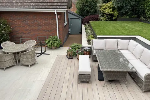 DesignBoard Composite decking in a light cinnamon tone forming a patio seating area, with rattan outdoor furniture and a raised lawn beyond.