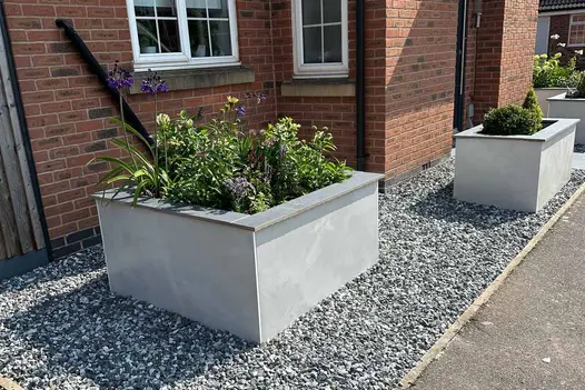 Valencia White Porcelain Cladding used to create crisp, modern planter walls at a front garden entrance, adding a clean contemporary finish against gravel beds and red brick façades.