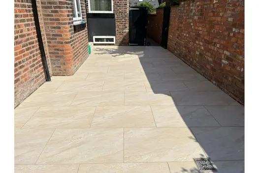 County Cream 900x600 Porcelain Paving against a red brick wall, creating a clean modern walkway.