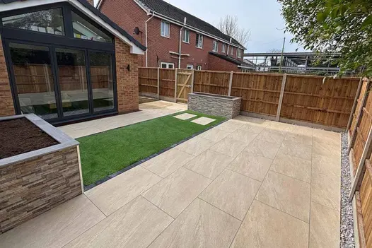 Clean and contemporary garden space paved with County Cream 900x600 porcelain slabs, complemented by raised planters and artificial grass.