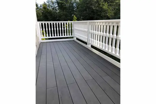 Dark Ash Brushed Composite Decking installed on an elevated terrace with white balustrade railing overlooking a green garden.