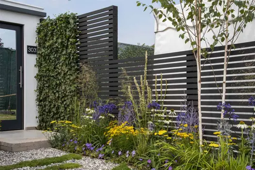 Dark Ash Composite Fence Battens installed as sleek horizontal screening behind lush border planting, providing a bold, modern backdrop in a landscaped garden.