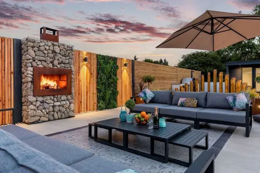 Outdoor living area with grey sofas and coffee table on patterned 600x600 Deco Porcelain tiles, set beside a rustic stone fireplace.