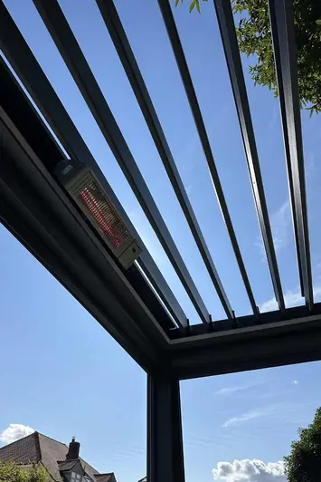 Close-up of the Deluxe Anthracite Grey metal Pergola's open louvres, framing a backdrop of trees and blue skies.