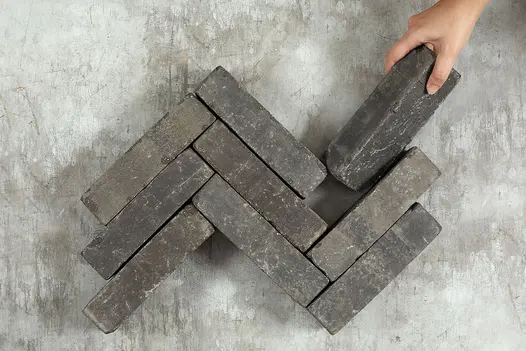 Hand places one Lucca clay paver against 8 matching patio bricks laid in 3 zigzag rows on pale background. Free UK delivery available.