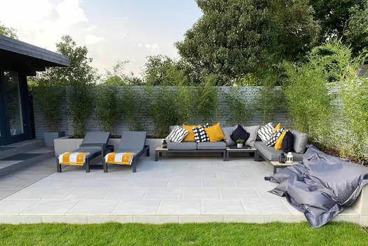 Florence Grey Porcelain paving forming a clean, modern terrace with grey outdoor loungers and a corner sofa, framed by tall bamboo planting.