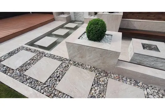 Contemporary outdoor space using Gaja Beige Porcelain, with decorative gravel, raised planters and geometric stepping stones.