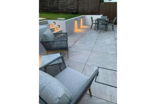 Modern outdoor living area paved with Gaja Grey Porcelain, featuring ambient lighting and grey lounge seating.