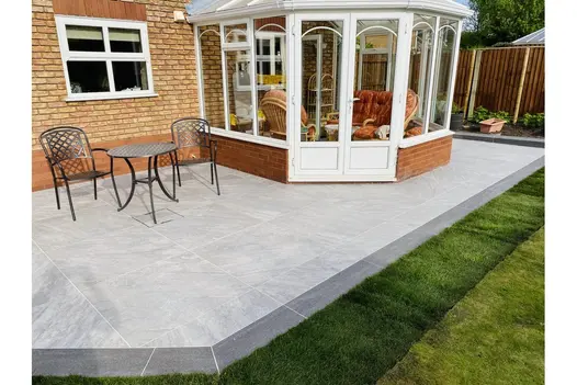 Garden patio using Gaja Grey 900x900 Porcelain Paving, with curved edge detail beside a conservatory.