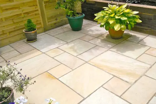 Mint Indian Sandstone Paving in soft cream and pale honey tones, laid in a random pattern on a sunny patio with potted plants and timber fencing.