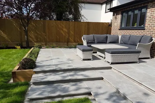 Graphite Grey Limestone paving used on a raised patio with wide steps, garden rattan seating and a lawn border.
