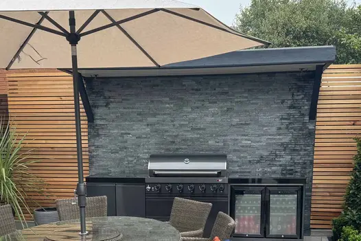 Green Slate Stone Cladding used as a feature backdrop in a modern outdoor kitchen, showcasing textured natural stone behind barbecue within a contemporary garden setting.