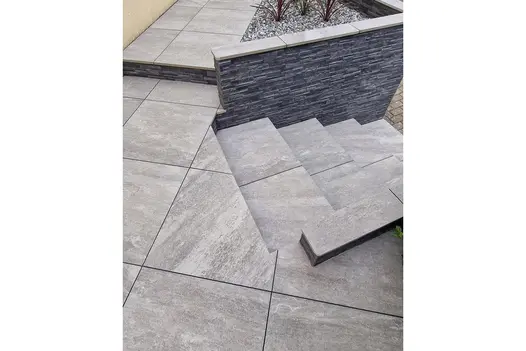 Tiered garden steps and patio area using Grey Quartz Porcelain Paving, bordered with a stone-clad retaining wall.