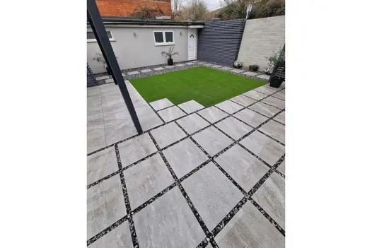 Modern garden with Grey Quartz 600x600 porcelain paving in grid pattern, artificial grass centre and dark stone border accents.