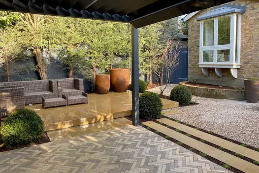 Gromo Antica Clay Brick Pavers laid in a herringbone pattern in contemporary setting, featuring a sheltered seating area, planters, gravel beds, and evergreen planting.