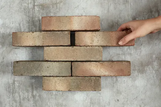 Hand adds 7th brick to 6 Bexhill clay pavers in alternating rows of 1 and 2 against pale background. Free UK delivery available.