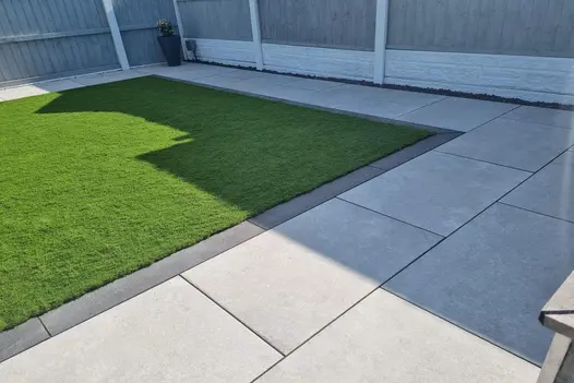 Lawn and patio combination with Heritage Grey Porcelain Paving, bordered by modern grey fencing.