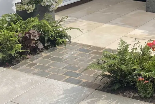 Tumbled Kandla Grey Sandstone Setts used as a small feature inset between planting and paving, showing their soft grey tones and weathered edges.