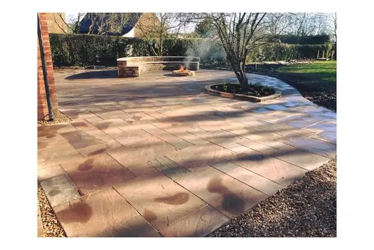 Expansive patio laid with Autumn Brown Sandstone in a traditional pattern, bordered by gravel and lawn.
